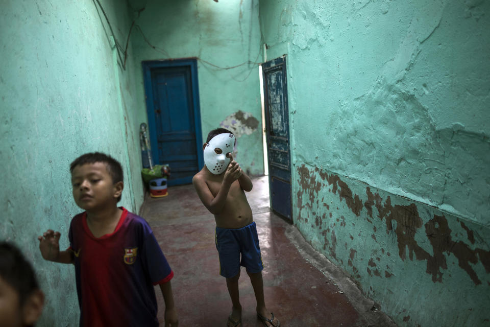 In this March 24, 2020 photo, children, one wearing a Jason Halloween mask, play inside the deteriorated house where they live nicknamed “Luriganchito,” after the country’s most populous prison, in Lima, Peru. The reference is not only because the residents are mostly ex-convicts, but also because the interior of the house is like a Latin American prison, with narrow passageways, without light and little air. (AP Photo/Rodrigo Abd)