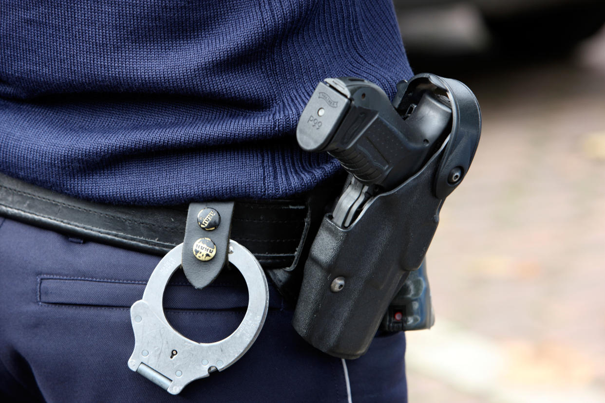 Police officer in blue uniform, with police gun, automatic, and handcuffs.