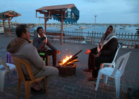 People sit around a fire as they wait for fishermen to come back with their catch, after Israel expanded fishing zone for Palestinians, at the seaport of Gaza City April 2, 2019. REUTERS/Suhaib Salem