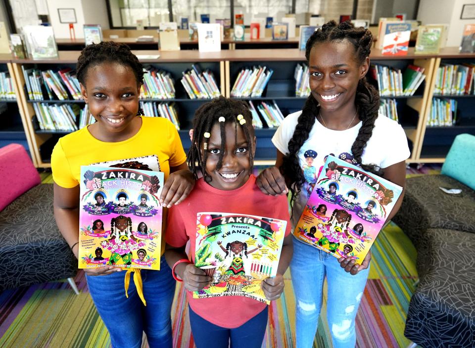 From left: Sisters Zakiya, Zahara and Zalika Obayuwana hold books they created in the school library at Ecole Kenwood French Immersion Elementary School in March. They will present their books Saturday at a book fair for new Americans, refugees, immigrants and others at the Karl Road branch library.
