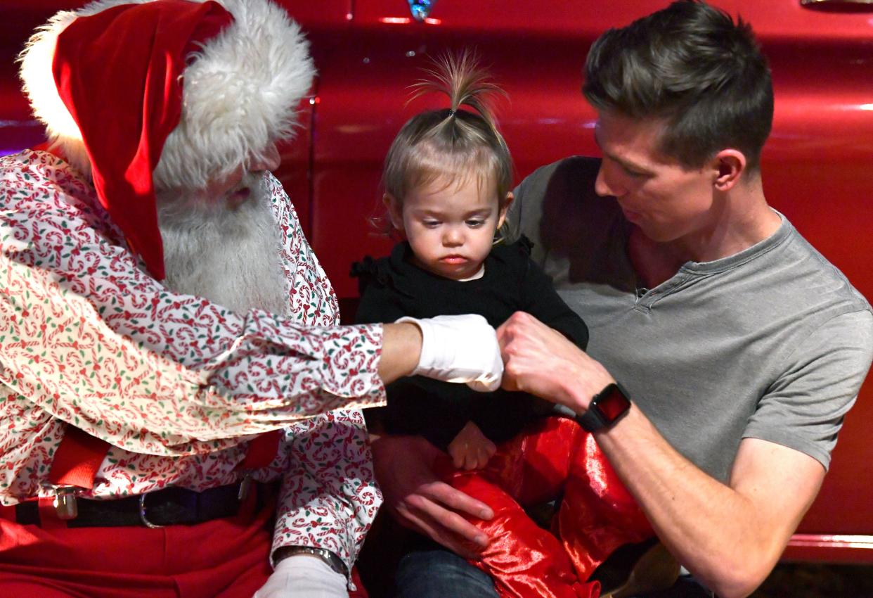 Everly Helmstadter, 2, watches as her father Josh tries to reassure her by fist-bumping Santa Claus while her mother, Aimee, takes their picture Friday. "Christmas in the Garden" was at Adamson-Spalding Storybook Garden beside the Abilene Convention Center.