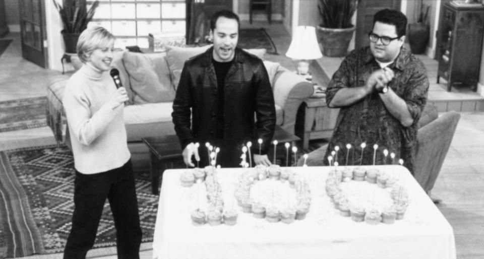 Ellen DeGeneres, Jeremy Piven, and David Anthony Higgins celebrate a milestone with a cake marked "100" in cupcakes, each with a lit candle