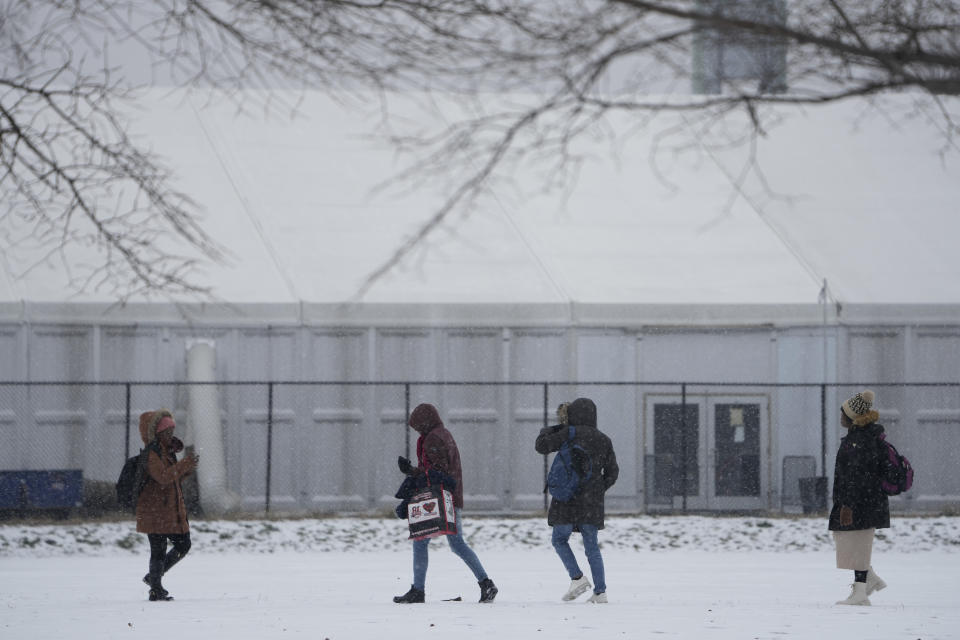 FILE - People walks across a snowy athletic field in front of a temporary shelter for migrants on Randall's Island in New York, Friday, Jan. 19, 2024. As New York City struggles to house an influx of immigrants, an unsanctioned tent community is growing outside the gates of the city's largest migrant shelter on Randall’s Island. New immigrants trying to earn a living have also set up a makeshift bazaar to sell coffee, snacks and other items. (AP Photo/Seth Wenig, File)