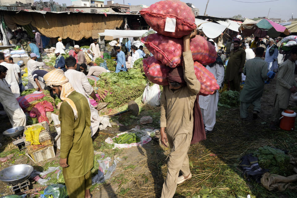 A Pakistani man, center, carries onion bags at vegetable market in Lahore, Pakistan, Wednesday, June. 12, 2024. (AP Photo/K.M. Chaudary)