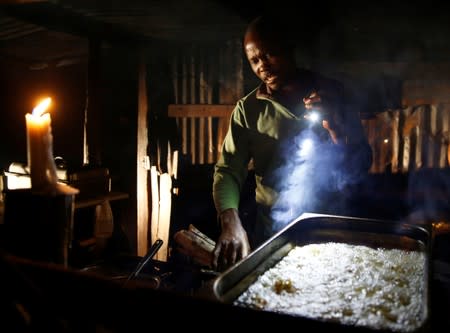 A street vendor prepares fried chips for sale using firewood, using candlelight and a cellphone, as the country faces 18-hour daily power cuts, in Harare