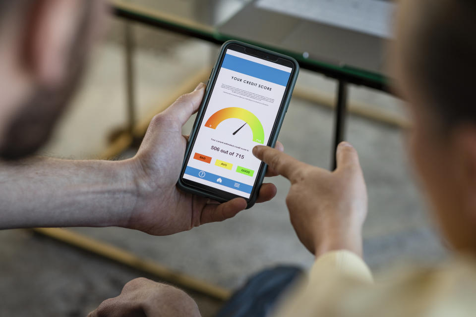 A high angle view of two unrecognisable friends sitting indoors, one man is holding a smart phone in his hand and they are looking at his credit score rating.