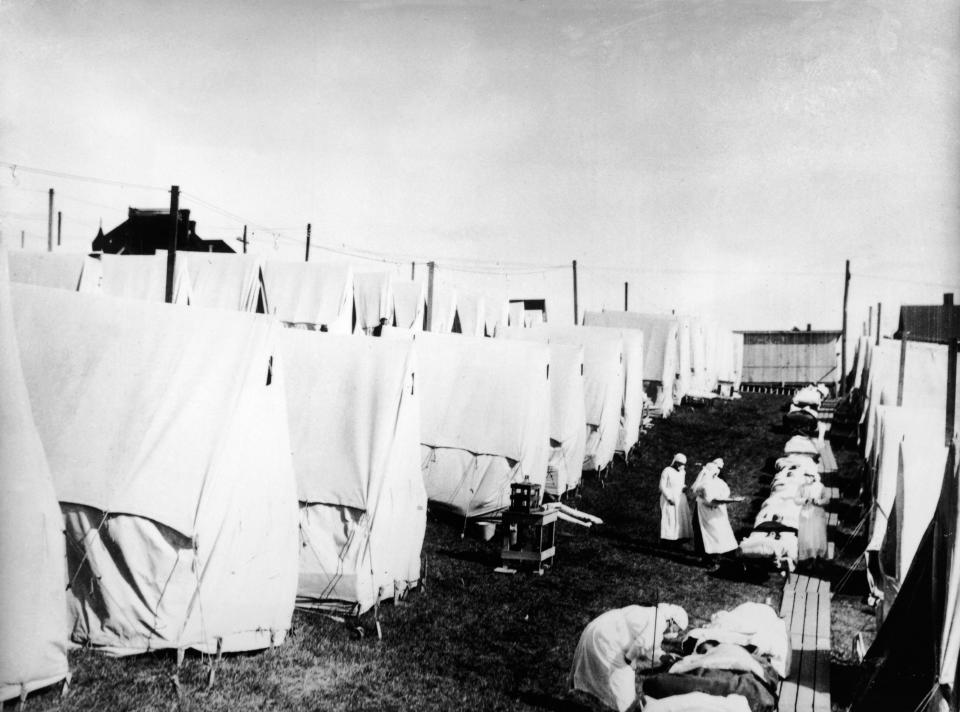 Masked doctors and nurses treat flu patients lying on cots and in outdoor tents at a hospital camp during the influenza epidemic of 1918. (Photo by Hulton Archive/Getty Images)