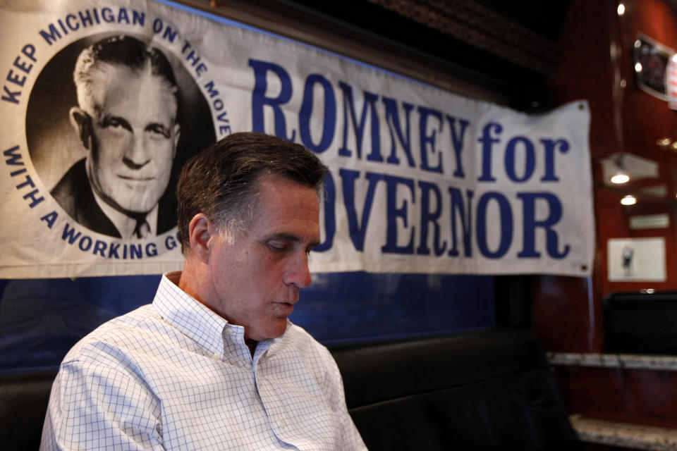 FILE - Republican presidential candidate, former Massachusetts Gov. Mitt Romney reads mail on his campaign bus between campaign stops in Monroe, Mich., and Farmington Hills, Mich., Feb. 16, 2012. Behind him is a campaign poster for his late father, George Romney, three-term Governor of Michigan. (AP Photo/Gerald Herbert, File)