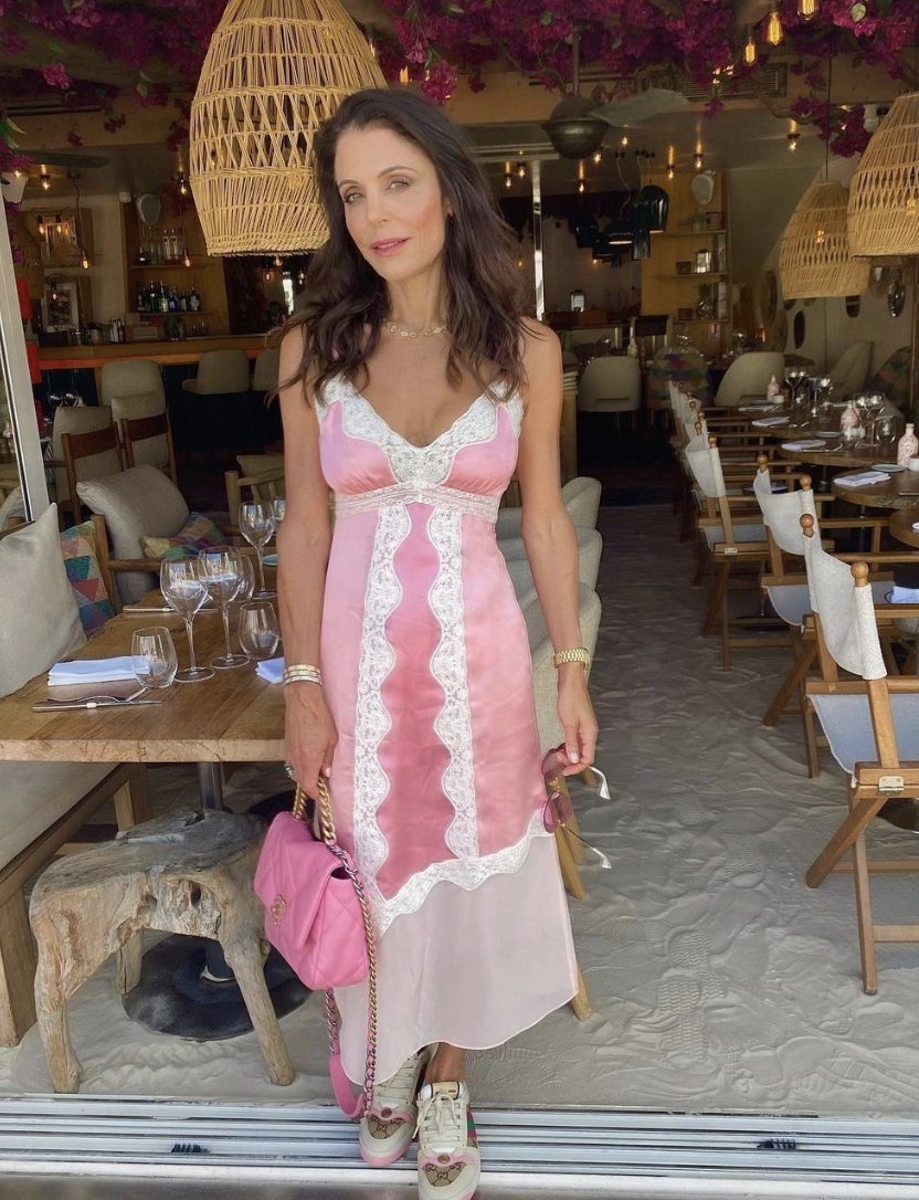 Bethenny Frankel stands at the door of a restaurant in a pink dress. 
