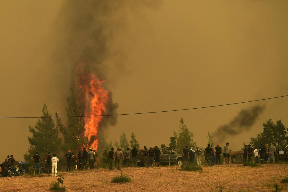 People watch the flames burning trees during a wildfire in Avgaria village on Evia island, about 184 kilometers (113 miles) north of Athens, Greece, Monday, Aug. 9, 2021. Firefighters and residents battled a massive forest fire on Greece's second largest island for a seventh day Monday, fighting to save what they can from flames that have decimated vast tracts of pristine forest, destroyed homes and businesses and sent thousands fleeing. (AP Photo/Michael Varaklas)