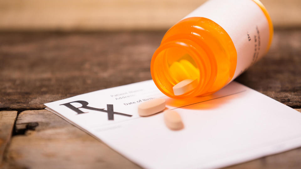 White, blank doctor's prescription pad with an orange prescription medication bottle lying on top of it with pills spilling out of the bottle.