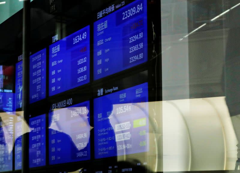 FILE PHOTO: People are reflected on a glass in front of a large screen showing stock prices at the Tokyo Stock Exchange after market opens in Tokyo