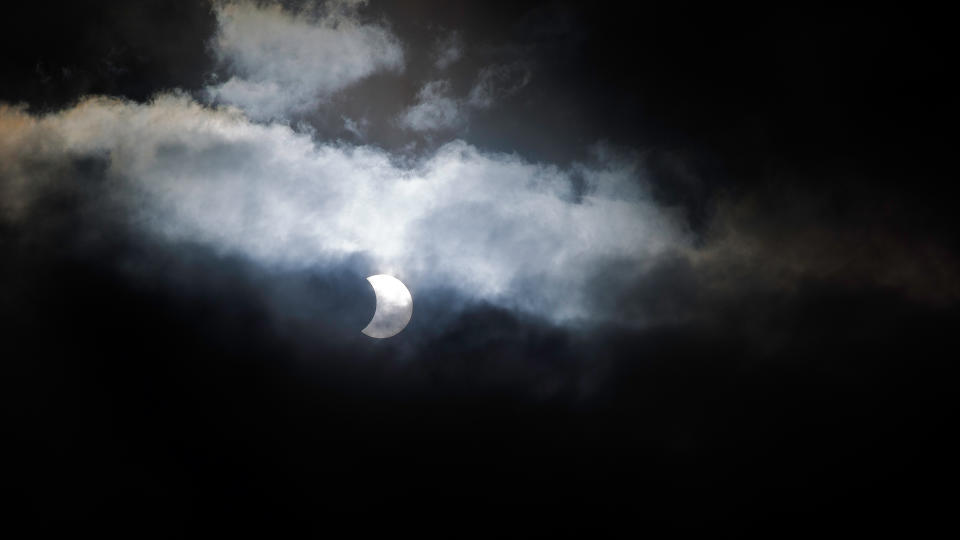 Solar eclipse through misty clouds and a dark sky.