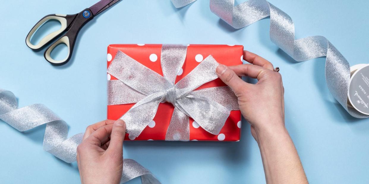 hands pulling ends of metallic ribbon gift wrapped in red and white polka dot wrapping paper