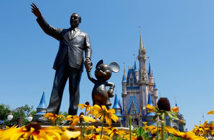 Statue of Walt Disney holding hands with Mickey Mouse, with Cinderella Castle in the background at Magic Kingdom, surrounded by flowers