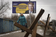 A woman passes by a board depicting former British Prime Minister Boris Johnson and reads: "The World of Brave People! #thank you for support", with antitank hedgehogs in the foreground, in the town of Bucha, outside Kyiv, Ukraine, Monday Jan. 30, 2023. (AP Photo/Efrem Lukatsky)
