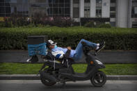 A delivery courier wearing a face mask to protect against the new coronavirus rests on his scooter in Beijing, Friday, July 3, 2020. Strict quarantine, social distancing and case tracing measures have helped radically bring down infections in China and mask wearing is still universal in indoor spaces, while many venues also require proof on a mobile phone app that the person is healthy. (AP Photo/Mark Schiefelbein)