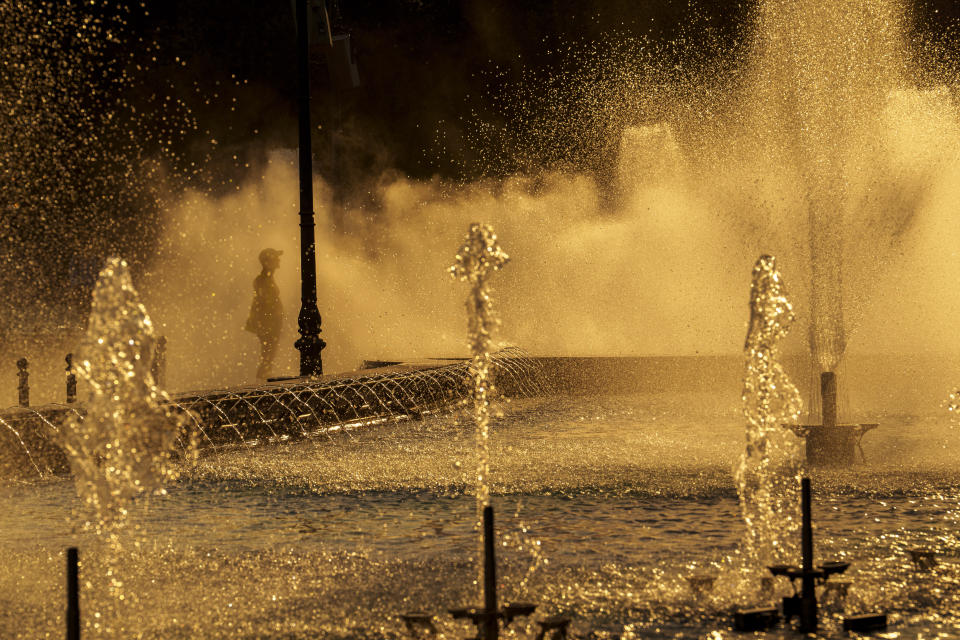 A municipal worker cools off standing next to a city fountain in Bucharest, Romania, Thursday, July 11, 2024, as temperatures exceeded 39 degrees Celsius (102.2 Fahrenheit). The national weather forecaster issued a red warning for the coming week, as temperatures are expected to exceed 40 degrees Celsius (104 Fahrenheit). (AP Photo/Vadim Ghirda)