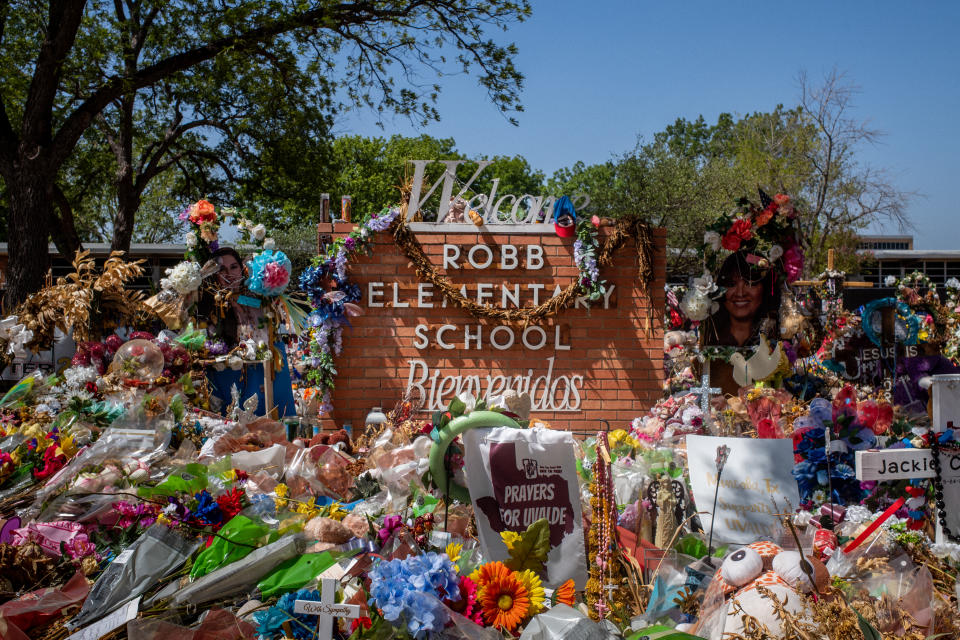 Flowers and gifts are piled around the Robb Elementary School sign.