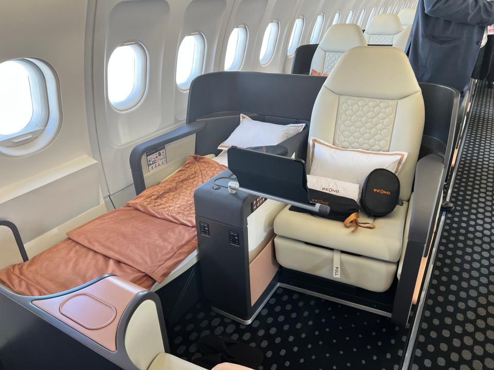 A seat on the Beond a319 is made up into a lie-down bed with an orange blanket and a white pillow.
