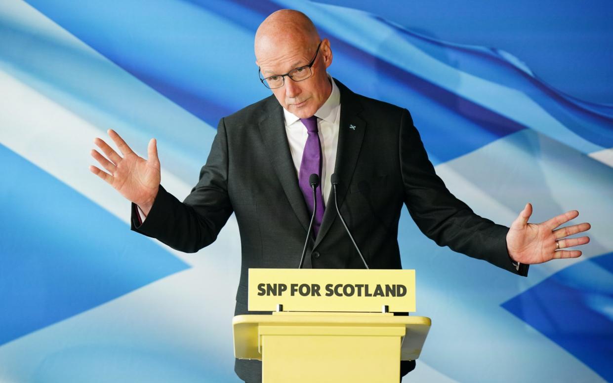 John Swinney gesticulates at a small podium