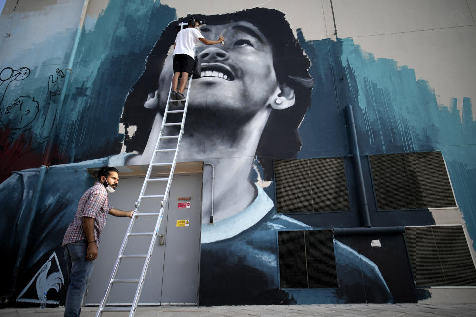 Workers paint a portrait of Argentinian soccer idol Diego Maradona in Doha, Qatar, Saturday, Nov. 19, 2022 ahead of the upcoming World Cup. (AP Photo/Christophe Ena)