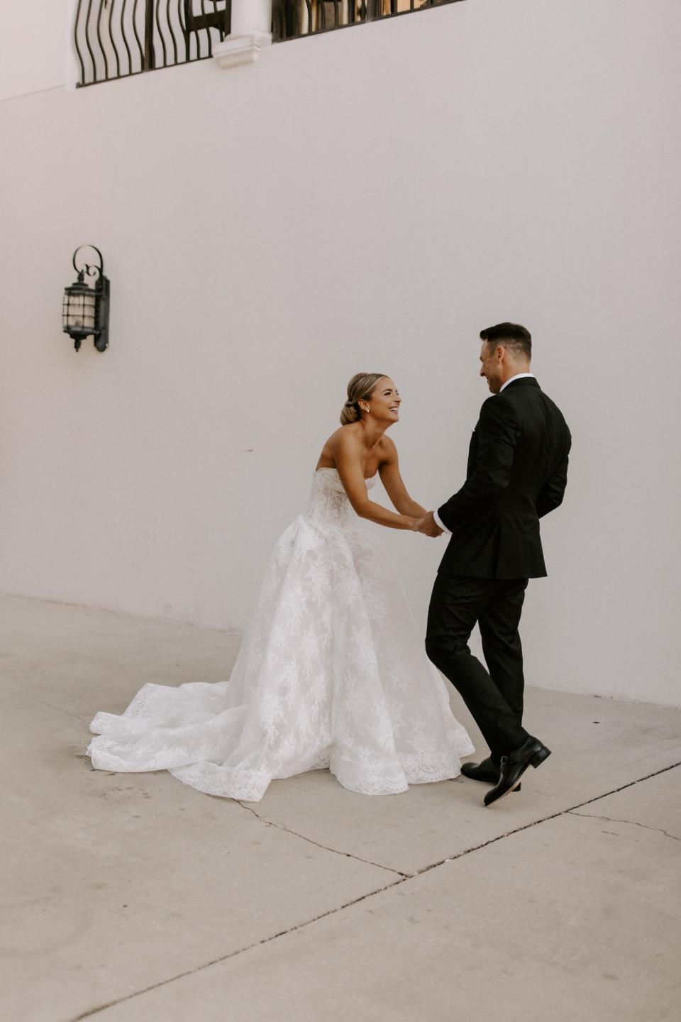 A bride laughs and holds hands with her groom in their wedding attire.