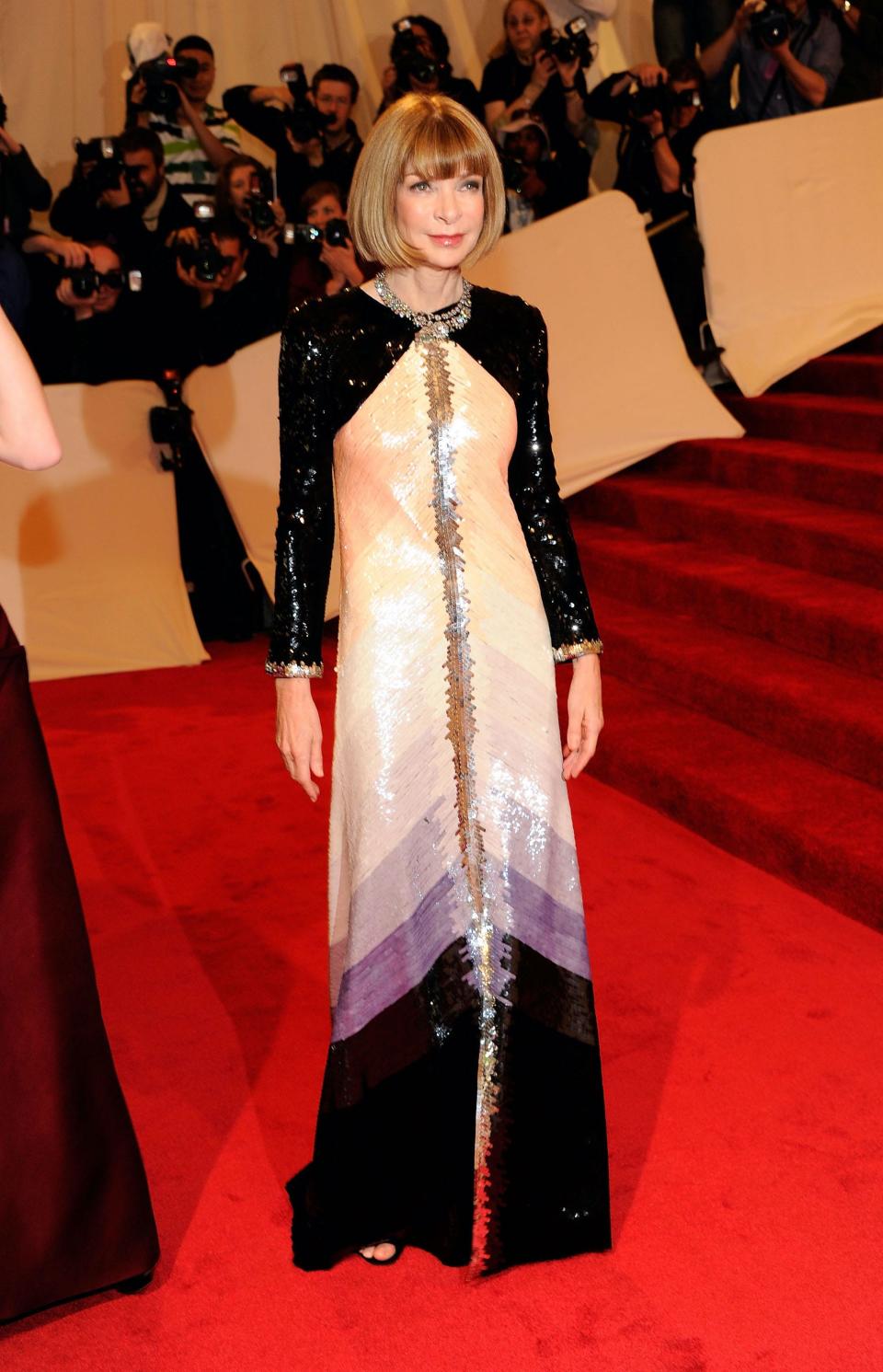 Anna Wintour wears a black and ombre long sleeve dress on a red carpet.