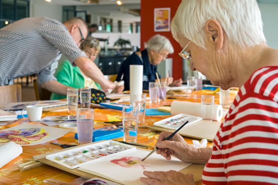 Seniors paint with watercolors with the help of an instructor.