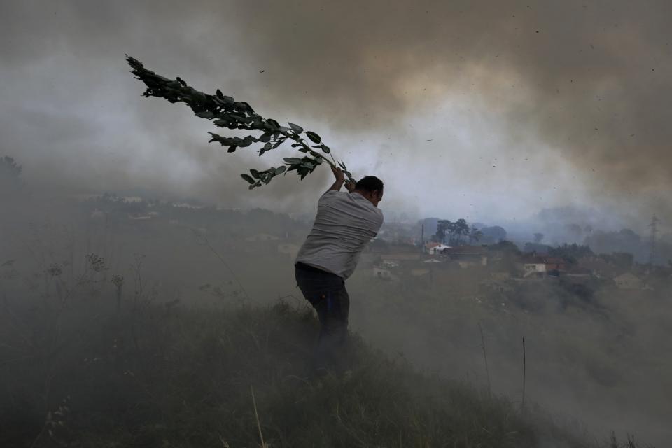 A volunteer swings a tree branch in an attempt to prevent a forest fire from reaching houses in the village of Casal da Quinta, outside Leiria, central Portugal, on July 12, 2022. (AP Photo/Joao Henriques)