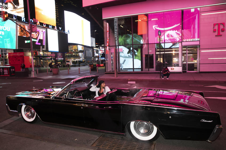 In this Saturday, May 2, 2020 photo, Tina Singh relaxes in a friend's 1967 Lincoln Continental in New York's Times Square during the coronavirus pandemic. Car mavens normally wouldn't dare rev their engines in Midtown, but now they're eagerly driving into the city to take photos and show off for sparse crowds walking through the commercial hub. (AP Photo/Mark Lennihan)