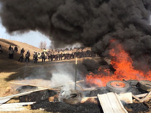 Tires burn as armed soldiers and law enforcement officers stand in formation to force Dakota Access pipeline protesters off private land. Source: AP