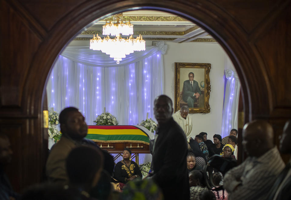 Family members and other mourners gather around the body of former president Robert Mugabe, whose portrait hangs on the wall, as he lies in state inside his official residence in the capital Harare, Zimbabwe Wednesday, Sept. 11, 2019. Zimbabwe's founding leader Robert Mugabe made his final journey back to the country Wednesday, his body flown into the capital amid the contradictions of his long, controversial rule. (AP Photo/Ben Curtis)