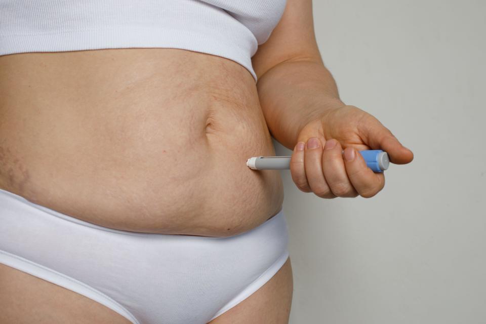 Woman making self injection with injection pen closeup. Medicine and treatment concept