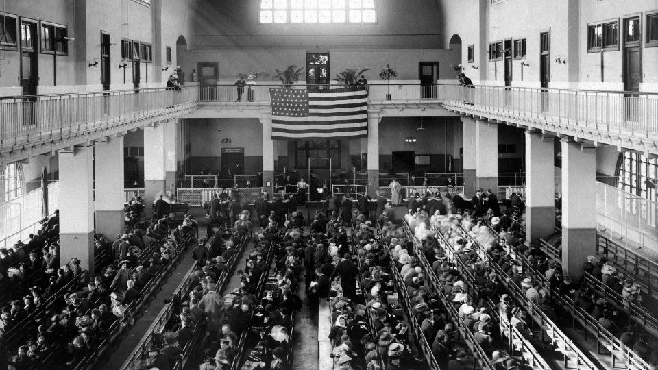 This 1907 photo shows the main hall of the United Station immigration inspection station on Ellis Island, where new immigrants lined the benches as they awaited processing and an American flag hung from the second floor. - Smith Collection/Gado/Archive Photos/Getty Images