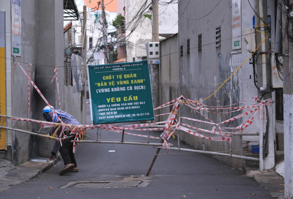 A man breaches through a barricade to get in an alley in Vung Tau, Vietnam, Monday, Sept. 20, 2021. The roadblocks and barricades make the streets of this southern Vietnamese city look like they did during the war that ended almost 50 years ago. But this time, the battle is being fought against the rampaging coronavirus.(AP Photo/Hau Dinh)