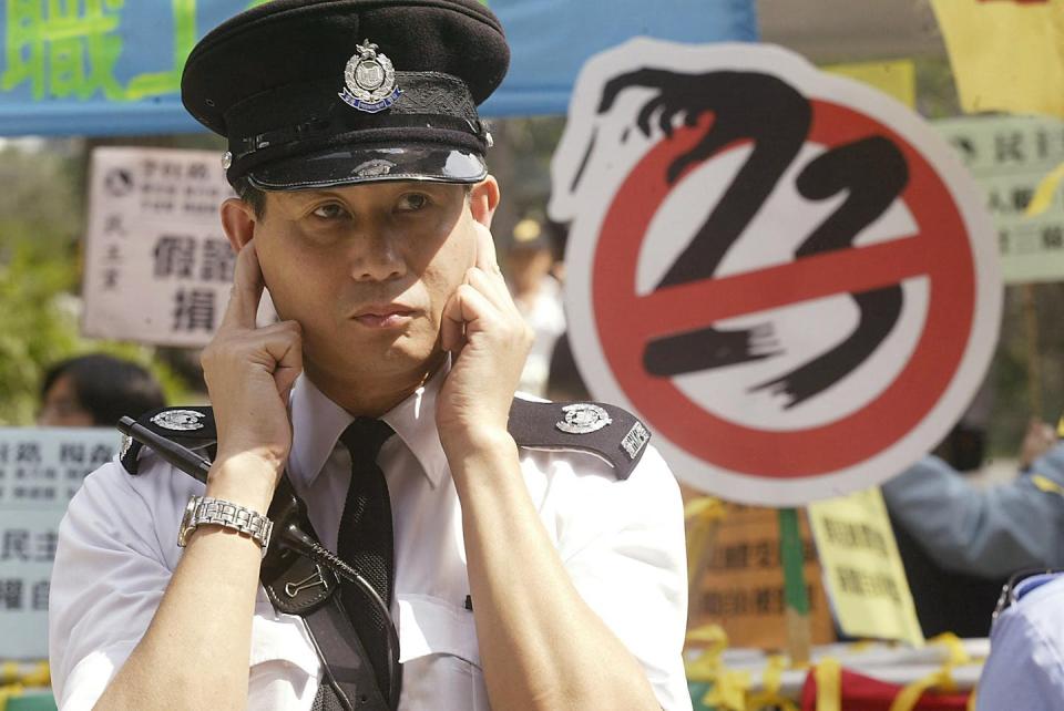 A uniformed police officer puts his fingers in his ears in front of a sign that has the number 23 crossed out.