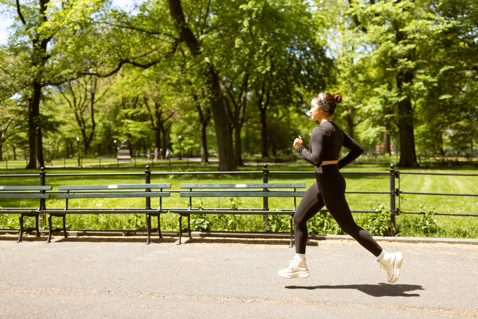 A person jogs in a park on a sunny day, with trees and benches in the background