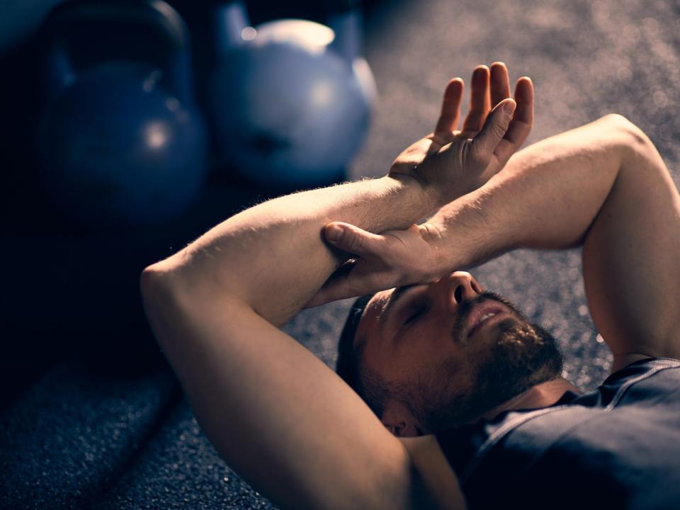 a tired athlete laying down on a gym floor next to kettlebell weights, exhausted after a workout