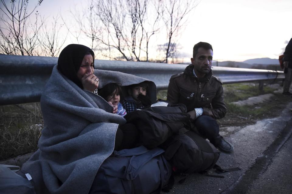 In this Sunday, Feb. 21, 2016 file photo, a woman cries as she and her children are covered with a blanket, near the northern Greek village of Idomeni. A tiny workshop charity called Naomi in the northern Greek city of Thessaloniki, is working long hours to collect and wash discarded blankets and turn them into wearable coats. The blankets are mostly army issue gray with red stitching and are distributed as aid at the sprawling refugee and migrant encampments, and are being recycled into practical coats for the vulnerable refugees who are facing a harsh winter. (AP Photo/Giannis Papanikos)