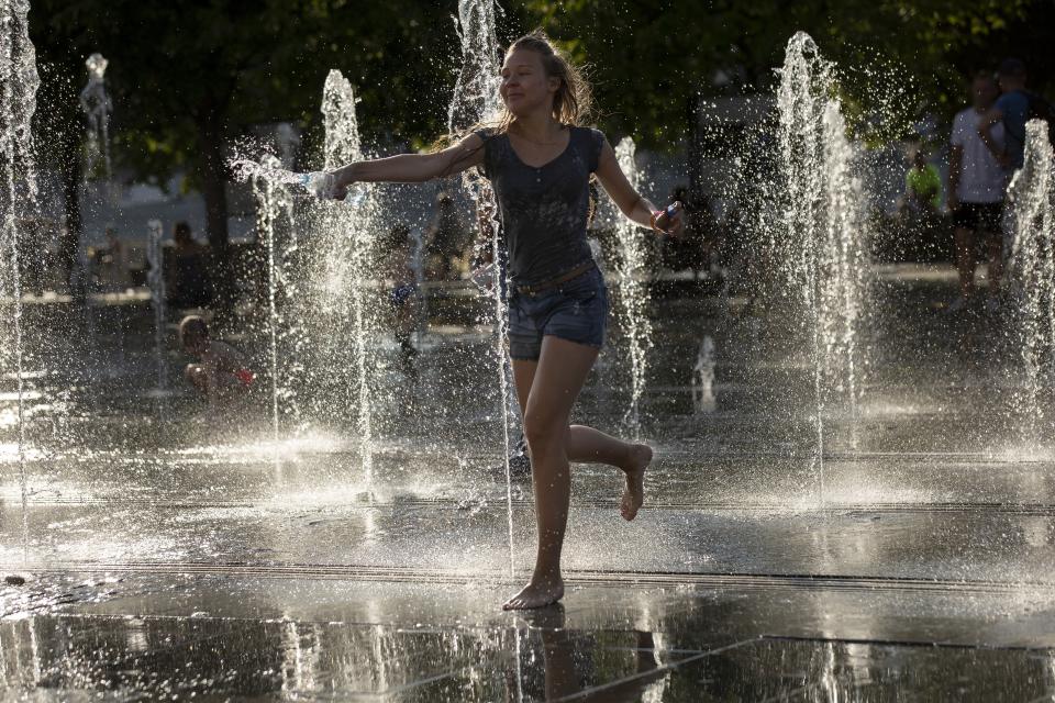 A woman cools herself running through a fountain at a park in Moscow, Russia, Friday, Aug. 3, 2018. The hot weather in Moscow is continuing, with temperatures forecast to reach 30 degrees Celsius (86 Fahrenheit) . (AP Photo/Alexander Zemlianichenko)