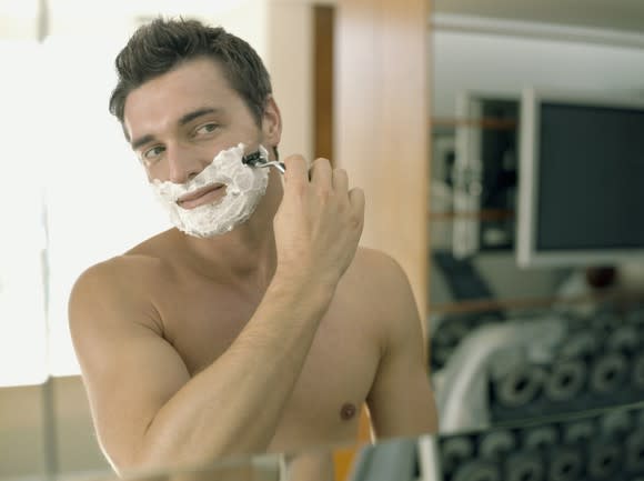 A man shaves in the mirror.