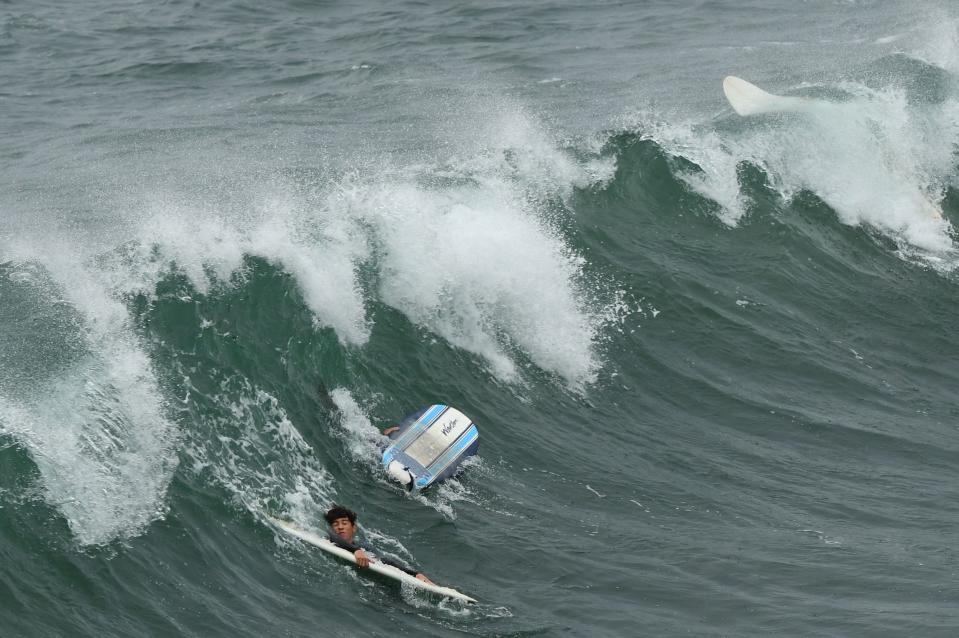 Surfers grip their surf boards in the middle of a wave in Manhattan Beach, California, on January 15, 2022.
