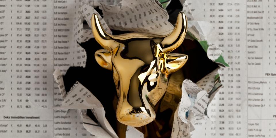 Detail of a golden bull breaking through the finance section of a newspaper - stock photo