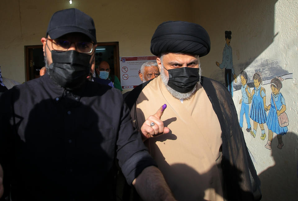 Populist Shiite cleric Muqtada al-Sadr, right, displays his ink-stained finger that shows he voted, at a polling center during the parliamentary elections in Najaf, Iraq, Sunday, Oct. 10, 2021. Iraq closed its airspace and land border crossings on Sunday as voters headed to the polls to elect a parliament that many hope will deliver much needed reforms after decades of conflict and mismanagement. (AP Photo/Anmar Khalil)