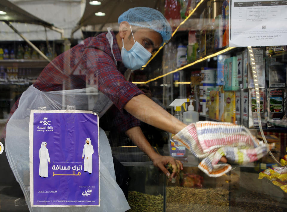 A worker wearing a face mask to help curb the spread of the coronavirus, wipes his shop window behind a poster emphasizing an enhanced social distancing campaign at a popular market in Jiddah, Saudi Arabia, Thursday, Dec. 17, 2020. The Arabic reads, "leave one meter distance." (AP Photo/Amr Nabil)