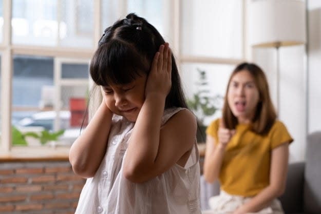 A young girl covers her ears as her mother yells at her