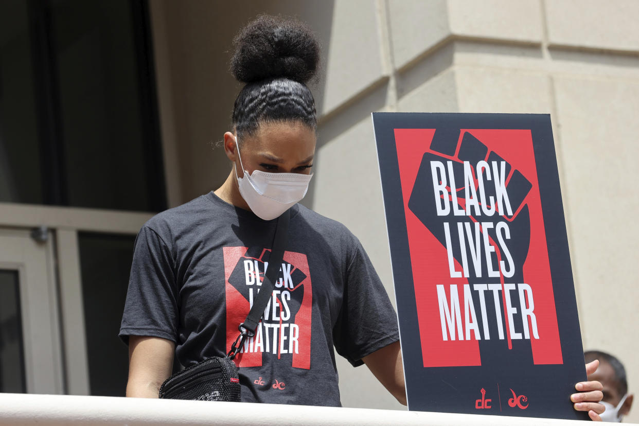 Natasha Cloud bows her head while holding a Black Lives Matter sign. She is wearing a shirt with the same logo.