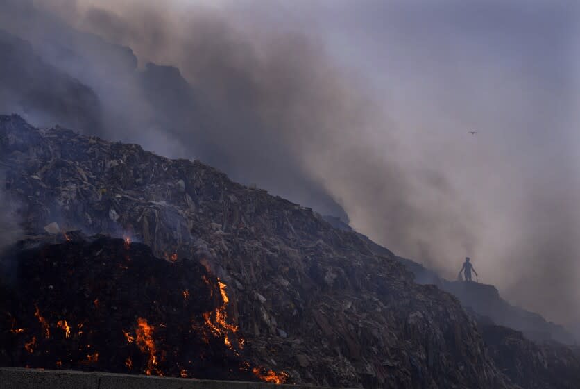 FILE - A person picks through trash for reusable items as a fire rages at the Bhalswa landfill in New Delhi, April 27, 2022. Landfills are releasing far more planet-warming methane into the atmosphere from the decomposition of waste than previously thought, a study suggests. Smoke hung over New Delhi for days after the massive landfill caught fire as the country was sweltering in an extreme heat wave. (AP Photo/Manish Swarup, File)