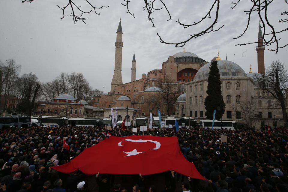 FILE - In this Saturday, March 16, 2019 file photo, backdropped by Hagia Sophia, the Byzantine-era cathedral that was turned into a mosque and now serves as a museum, demonstrators protest holding a Turkish flag. The 6th-century building is now at the center of a heated debate between conservative groups who want it to be reconverted into a mosque and those who believe the World Heritage site should remain a museum. (AP Photo/Lefteris Pitarakis, File)